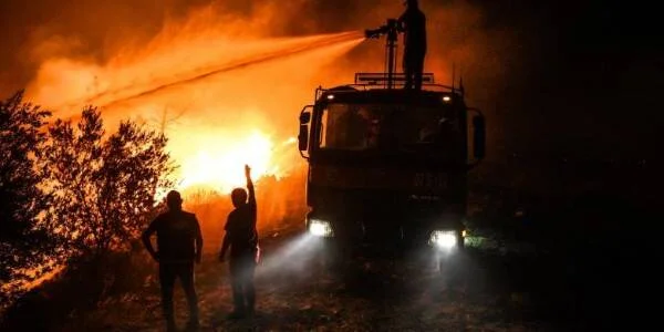 Bomberos y camión cisterna lanzan agua sobre un incendio forestal en la noche entre intensas llamas.