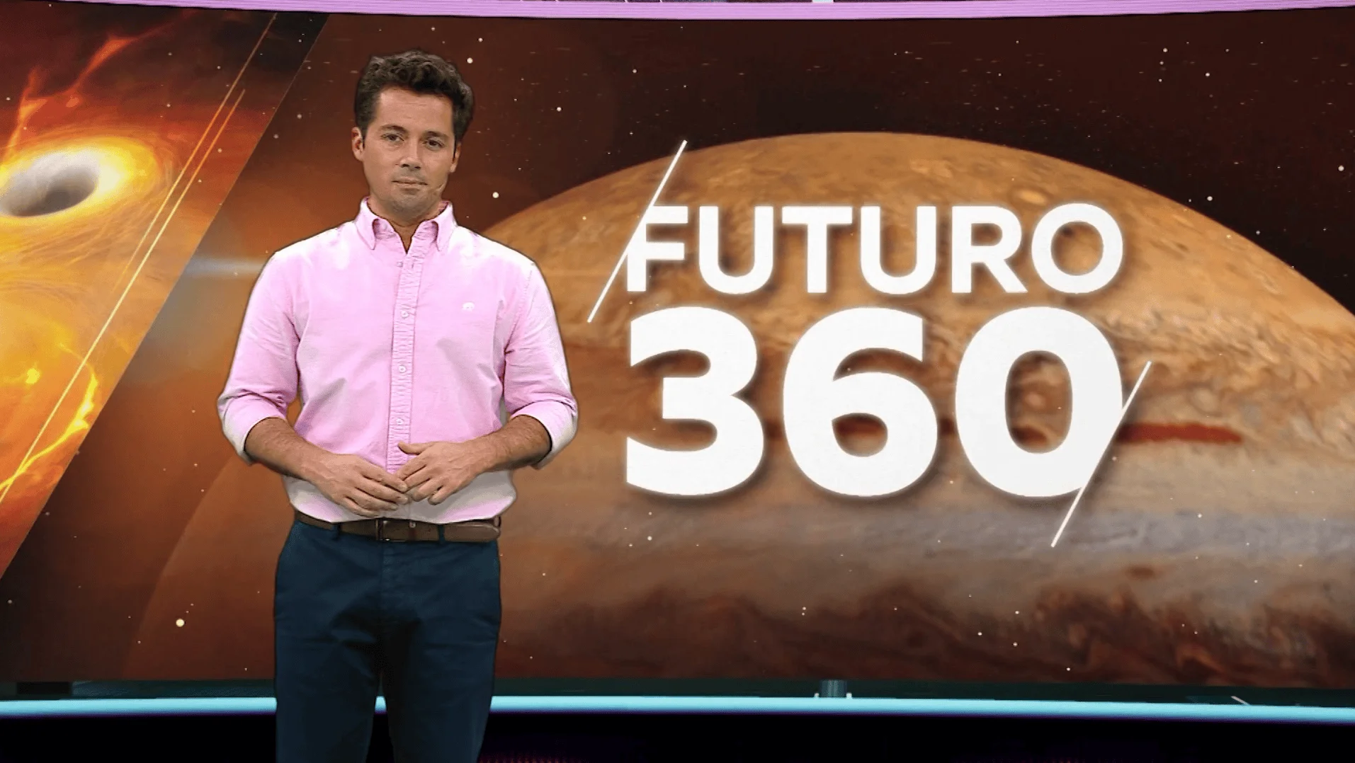 Conductor de camisa rosa de pie frente a una pantalla con el logotipo del programa televisivo Futuro 360 y imágenes del espacio.