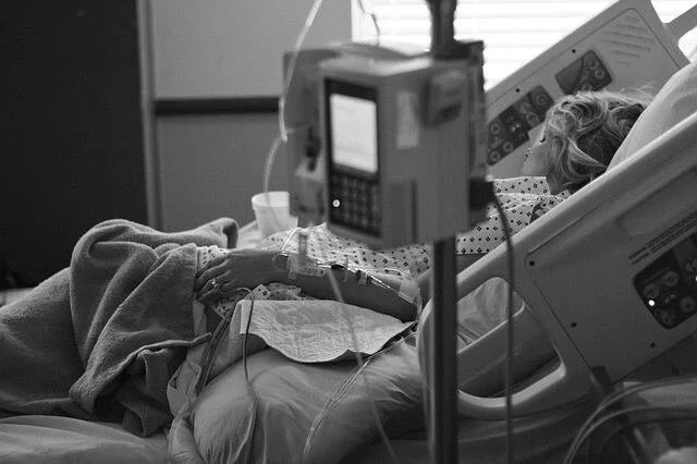 Mujer recostada en cama de hospital con vías intravenosas y bomba de infusión conectada.