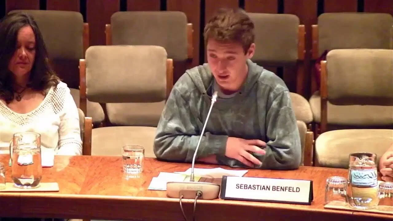 Sebastian Benfeld habla frente a un micrófono en una mesa de conferencia durante un panel formal.