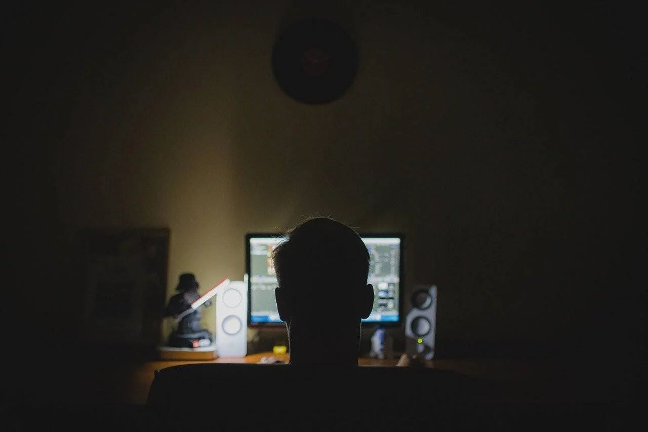 Silueta de una persona trabajando ante dos monitores encendidos en una habitación a oscuras.