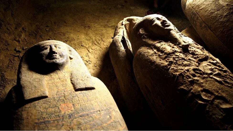 Varios sarcófagos antropomorfos del antiguo Egipto con rostros tallados, hallados en el interior de una tumba oscura.