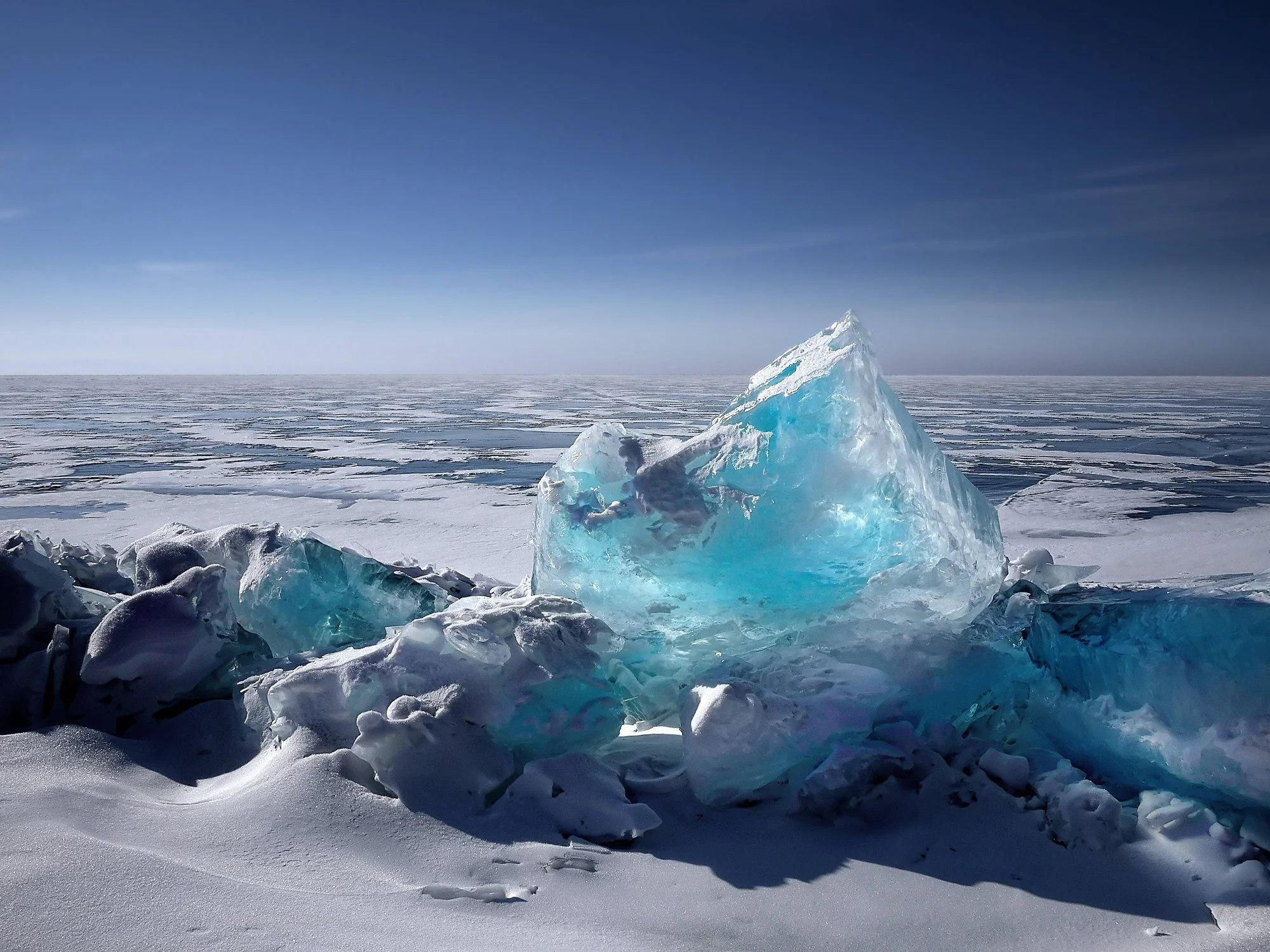 Gran bloque de hielo translúcido de color azul turquesa sobre una extensa llanura de hielo y nieve bajo un cielo despejado.
