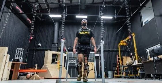 Soldado con camiseta del Army prueba un exoesqueleto en las piernas dentro de un laboratorio de biomecánica militar.