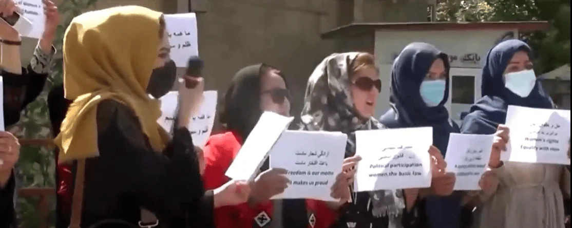 Grupo de mujeres con hiyab sostienen carteles en dari e inglés exigiendo derechos políticos y libertad en una protesta callejera.
