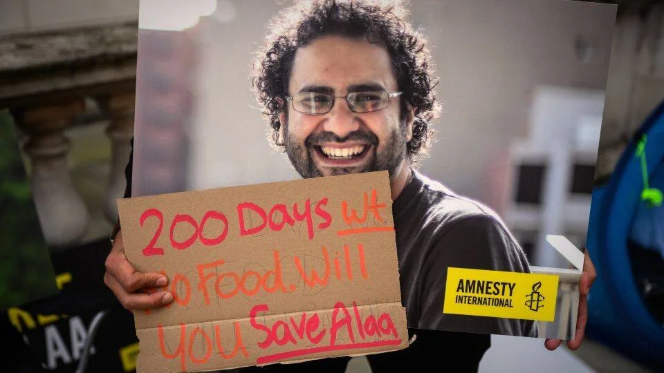 Manifestante sostiene cartel de Amnesty International con foto de un hombre y el texto '200 Days Without Food, Will You Save Alaa'.