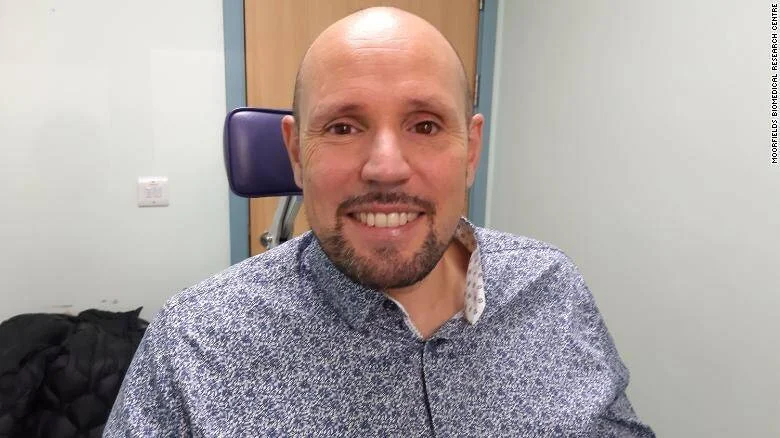 Hombre calvo con barba sonríe en una sala del Moorfields Biomedical Research Centre.