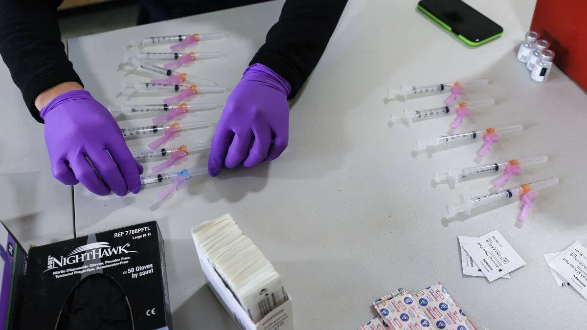 Persona con guantes morados organiza filas de jeringas sobre una mesa junto a guantes desechables y apósitos.