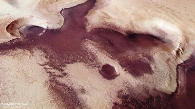 Vista aérea de la superficie de Marte con tonos rojizos, depósitos de hielo blanco y formaciones rocosas del terreno marciano.