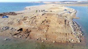 Vista aérea de ruinas de una ciudad antigua expuestas en una península rodeada de agua, con arqueólogos trabajando en el sitio.