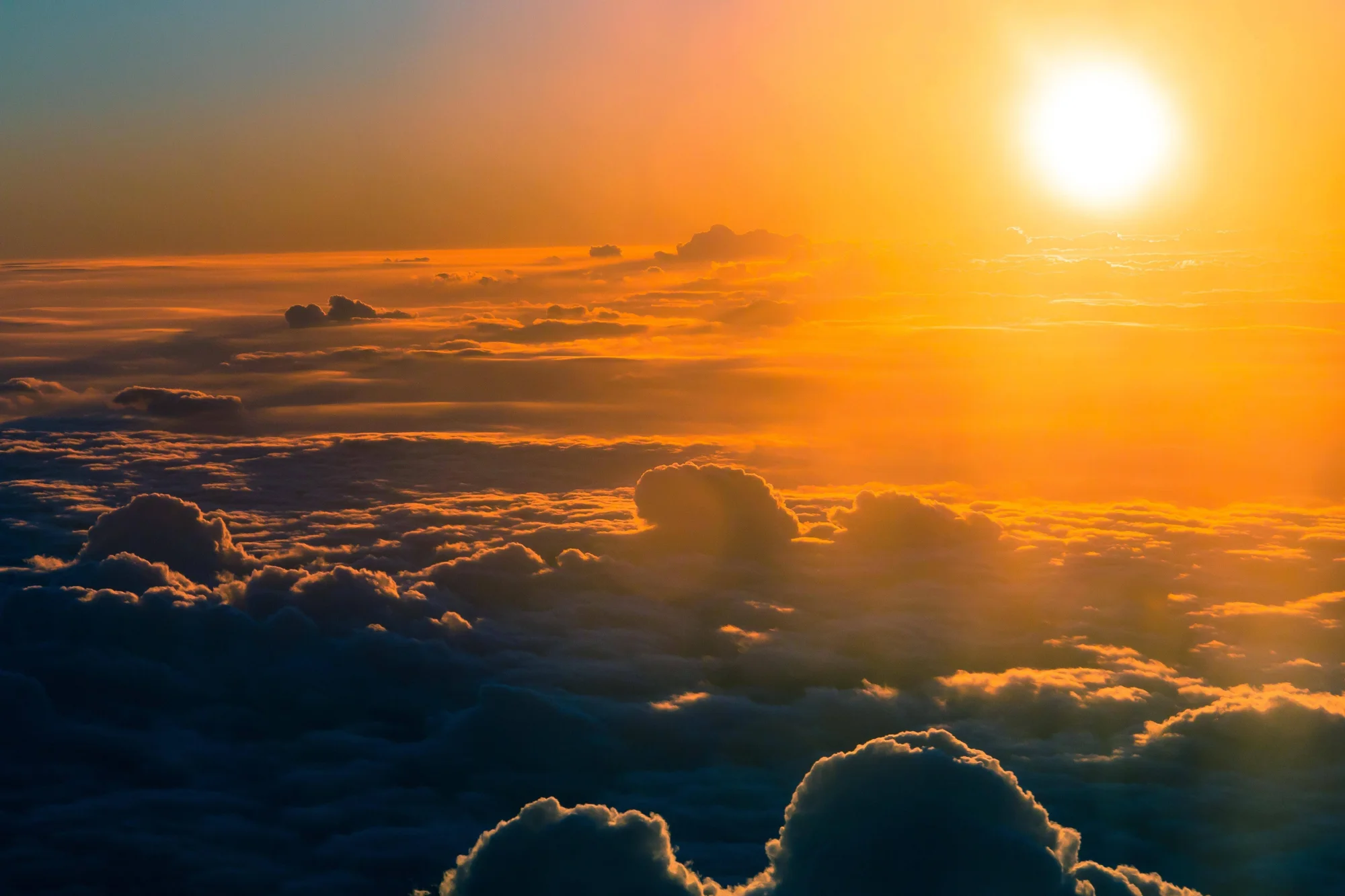 Vista aérea de un amanecer con el sol brillante en tonos naranja y dorado sobre un extenso mar de nubes.