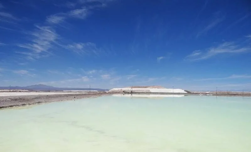 Piletas de salmuera turquesa para extracción de litio en un salar desértico, con montañas y cielo azul al fondo.