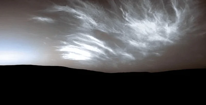 Nubes wispy iluminadas sobre el horizonte oscuro de Marte, captadas por un róver en la superficie del planeta.