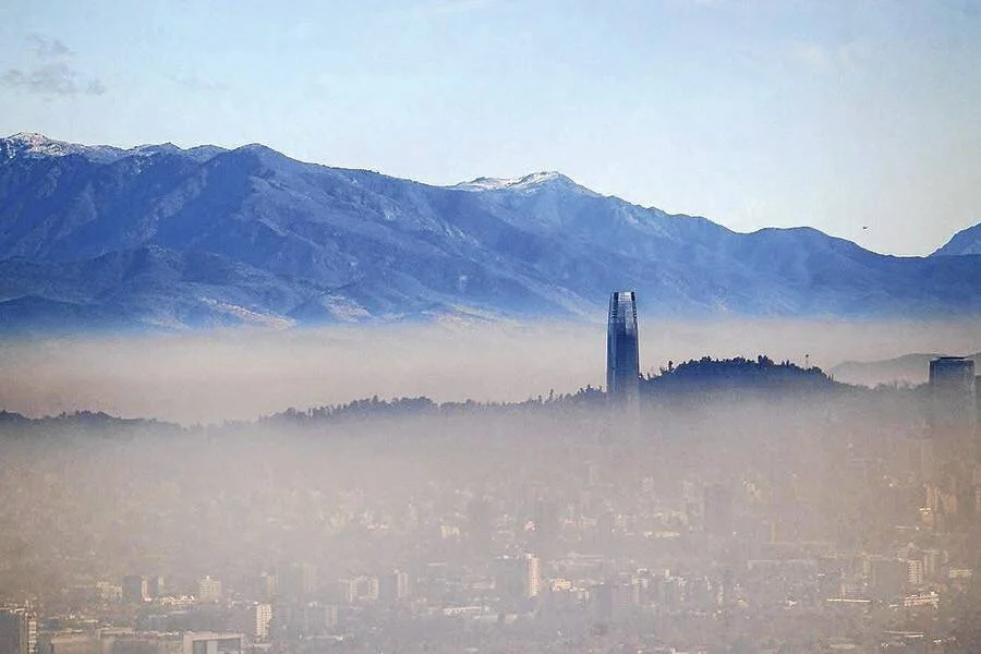 Capa de smog cubre una ciudad con una torre alta emergiendo, y montañas nevadas de fondo.