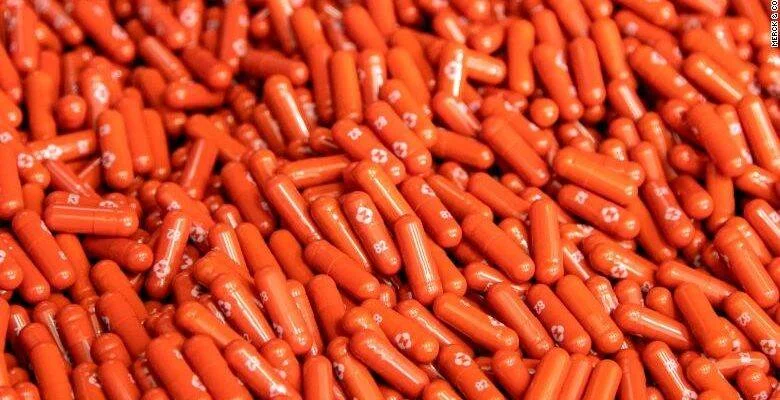 Gran cantidad de cápsulas farmacéuticas de color naranja con logotipo de Merck dispersas sobre una superficie.