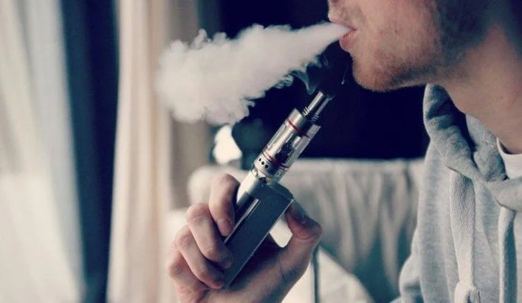 Hombre exhala una gran nube de vapor mientras usa un cigarrillo electrónico tipo mod.