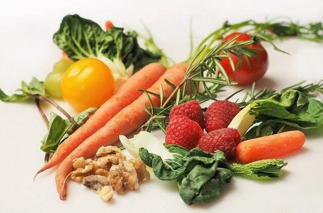 Zanahorias, frambuesas, tomate, pimiento amarillo, nueces, espinacas y romero dispuestos sobre fondo blanco.