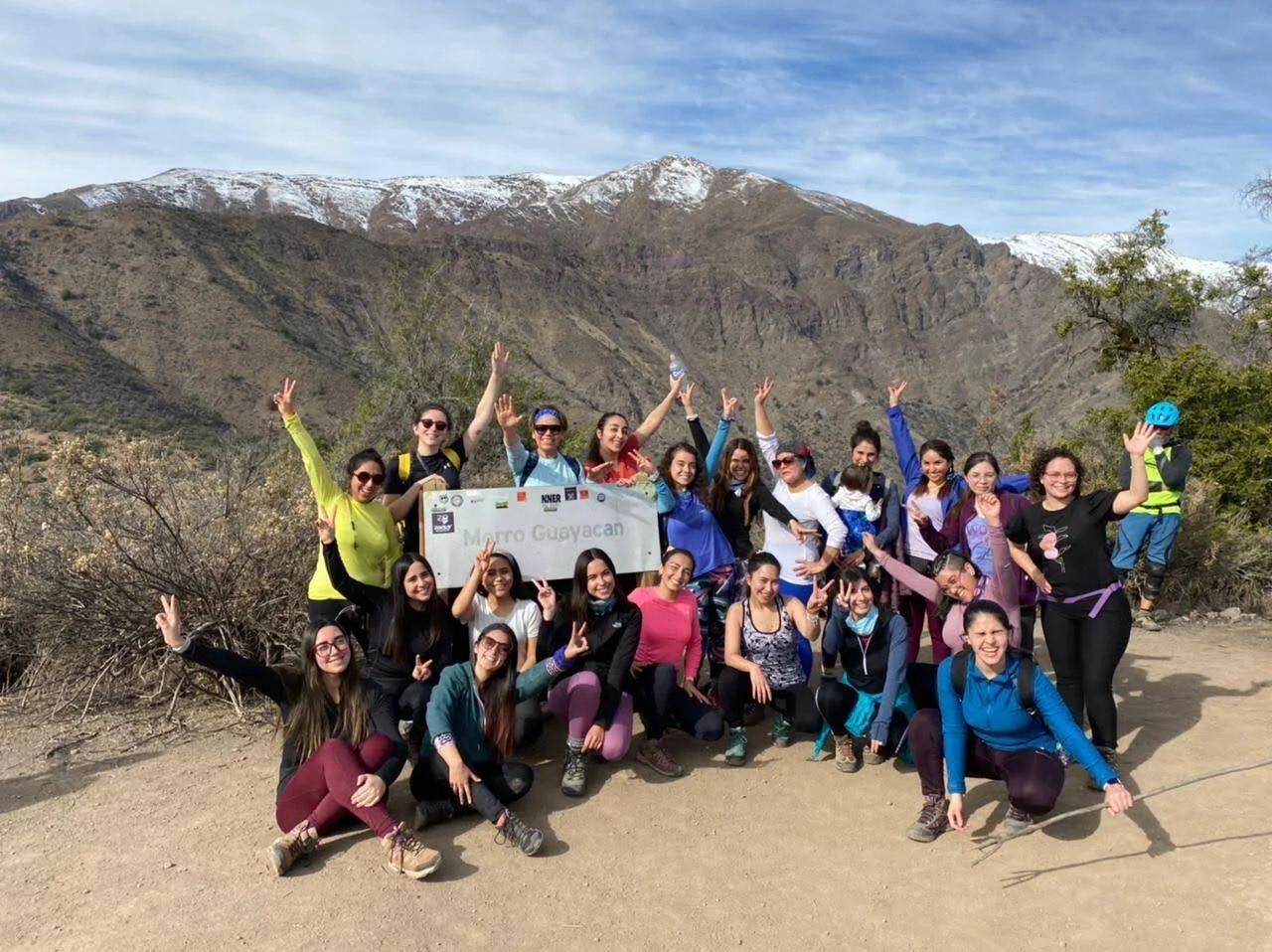 Grupo de mujeres posan celebrando junto al letrero del Morro Guayacán, con montañas nevadas al fondo.