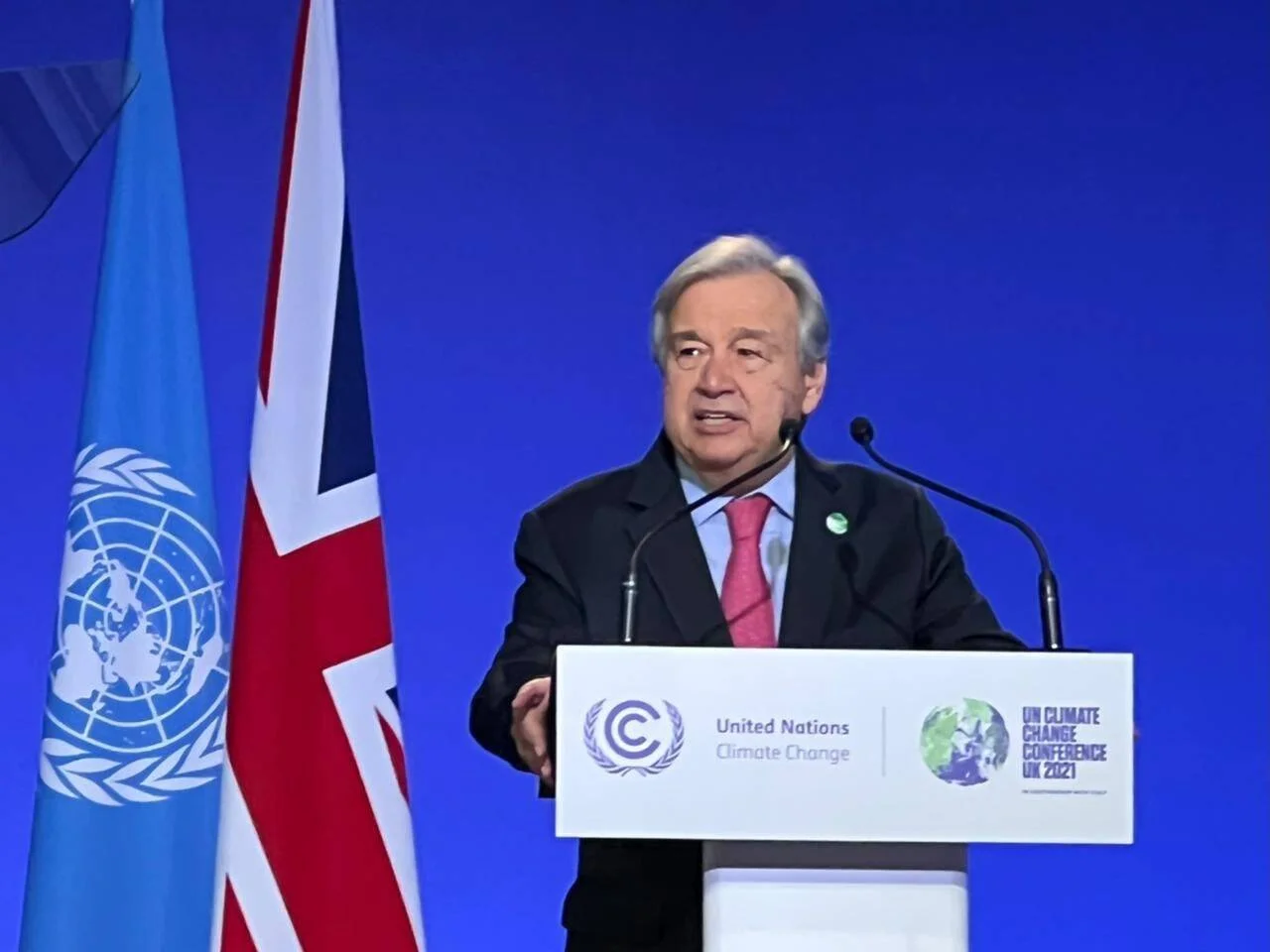 Hombre discursa en el podio de la Conferencia de Cambio Climático de la ONU UK 2021, con banderas de la ONU y del Reino Unido al fondo.