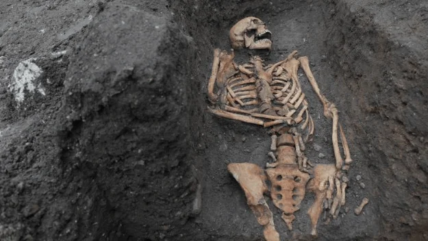 Esqueleto humano completo en posición supina dentro de una fosa de tierra oscura durante una excavación arqueológica.