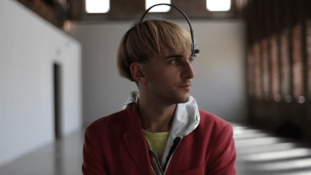 Joven de cabello rubio con un dispositivo de interfaz cerebro-computadora colocado sobre la cabeza, mirando hacia un lado.
