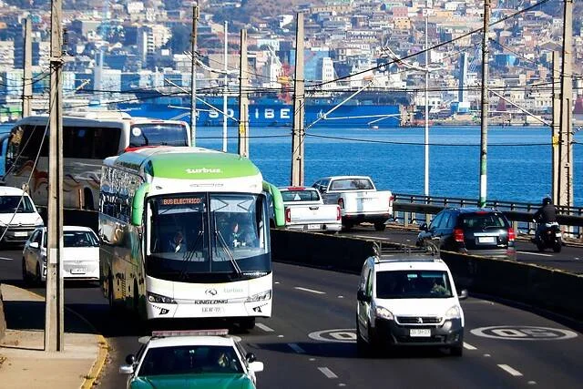 Bus eléctrico de Turbus circula por una avenida con vista al puerto y cerros de Valparaíso al fondo.