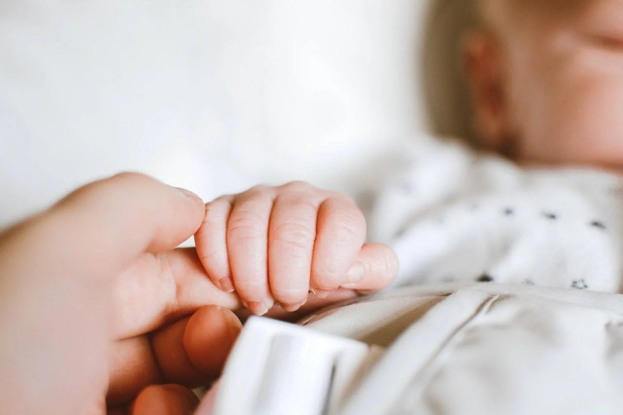 La pequeña mano de un bebé recién nacido aprieta el dedo de un adulto mientras duerme.