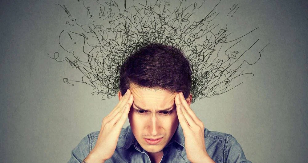 Hombre con expresión angustiada sostiene su cabeza entre las manos mientras líneas caóticas emergen de su mente, simbolizando el estrés o la ansiedad.
