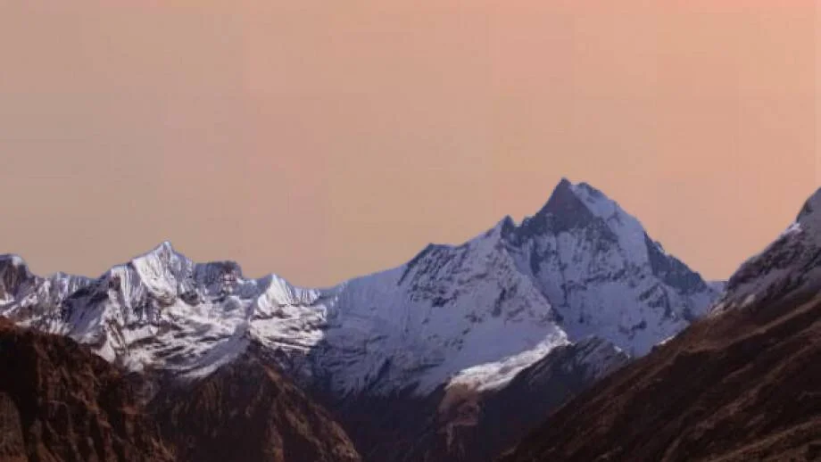 Cadena montañosa con picos nevados bajo un cielo de tonos rosados al atardecer.