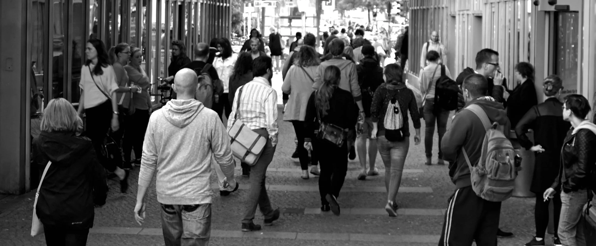 Numerosas personas caminan en ambas direcciones por una concurrida calle peatonal urbana, en blanco y negro.