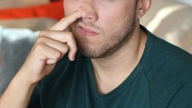 Hombre joven con remera verde oscuro apoya el dedo en la nariz con expresión pensativa.