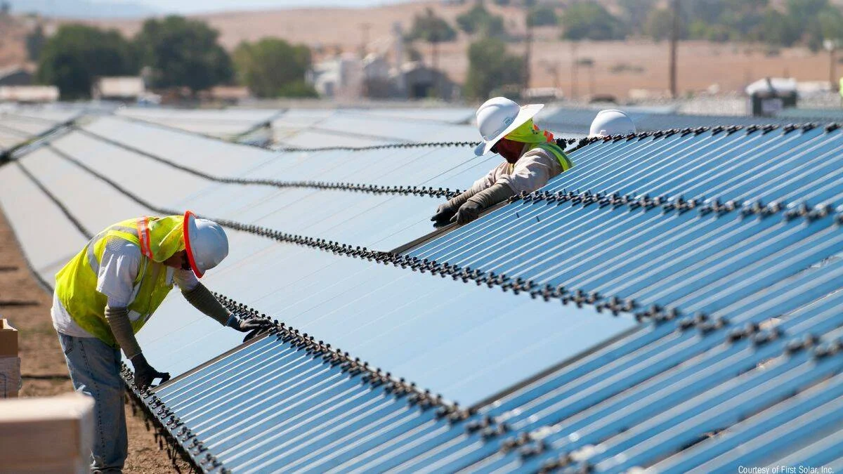 Dos técnicos con cascos y chalecos de seguridad instalan paneles solares en una gran planta fotovoltaica a campo abierto.
