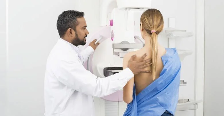 Médico con guardapolvo blanco asiste a una mujer durante un estudio de mamografía en un centro médico.