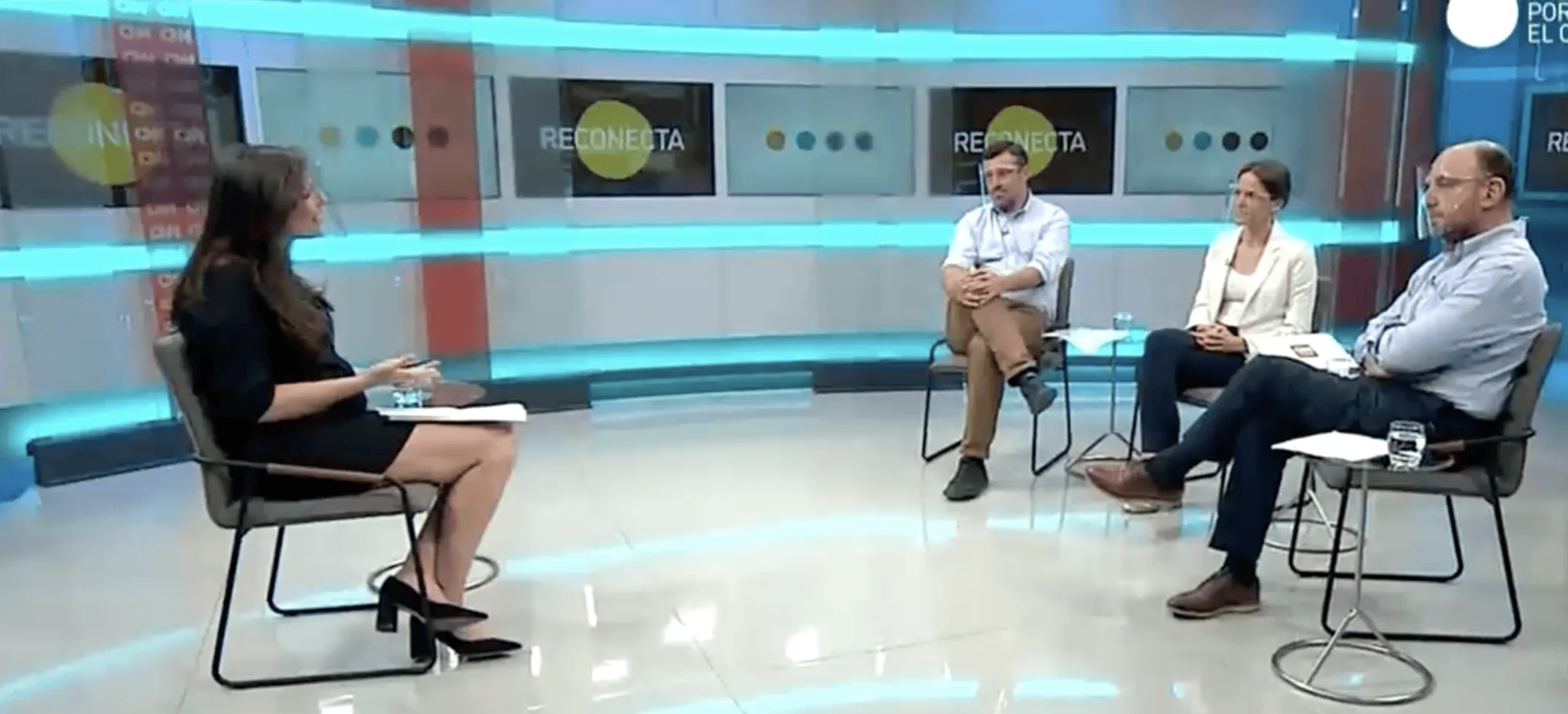 Una conductora entrevista a tres panelistas sentados en un estudio de televisión con el logo 'Reconecta' al fondo.