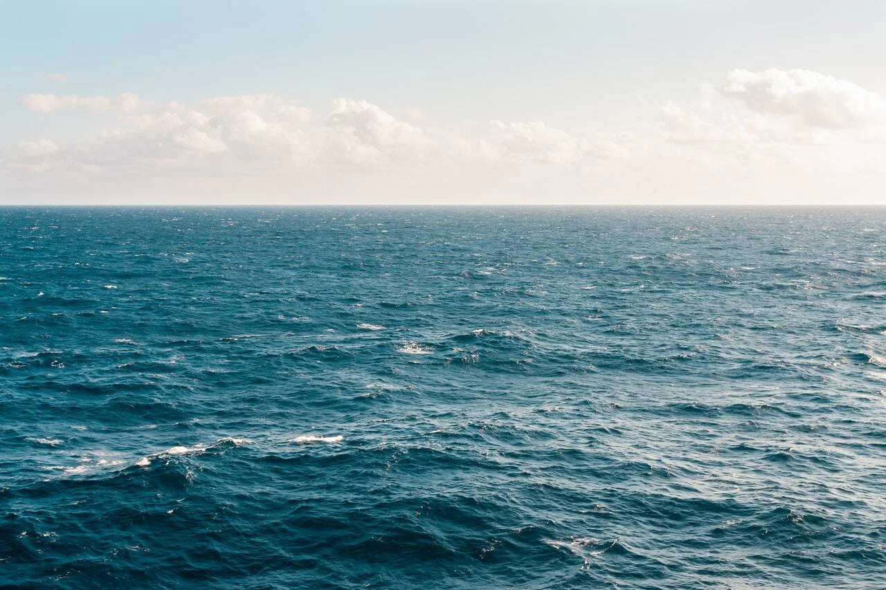 Extensión de océano azul con olas suaves bajo un cielo parcialmente nublado y horizonte despejado.