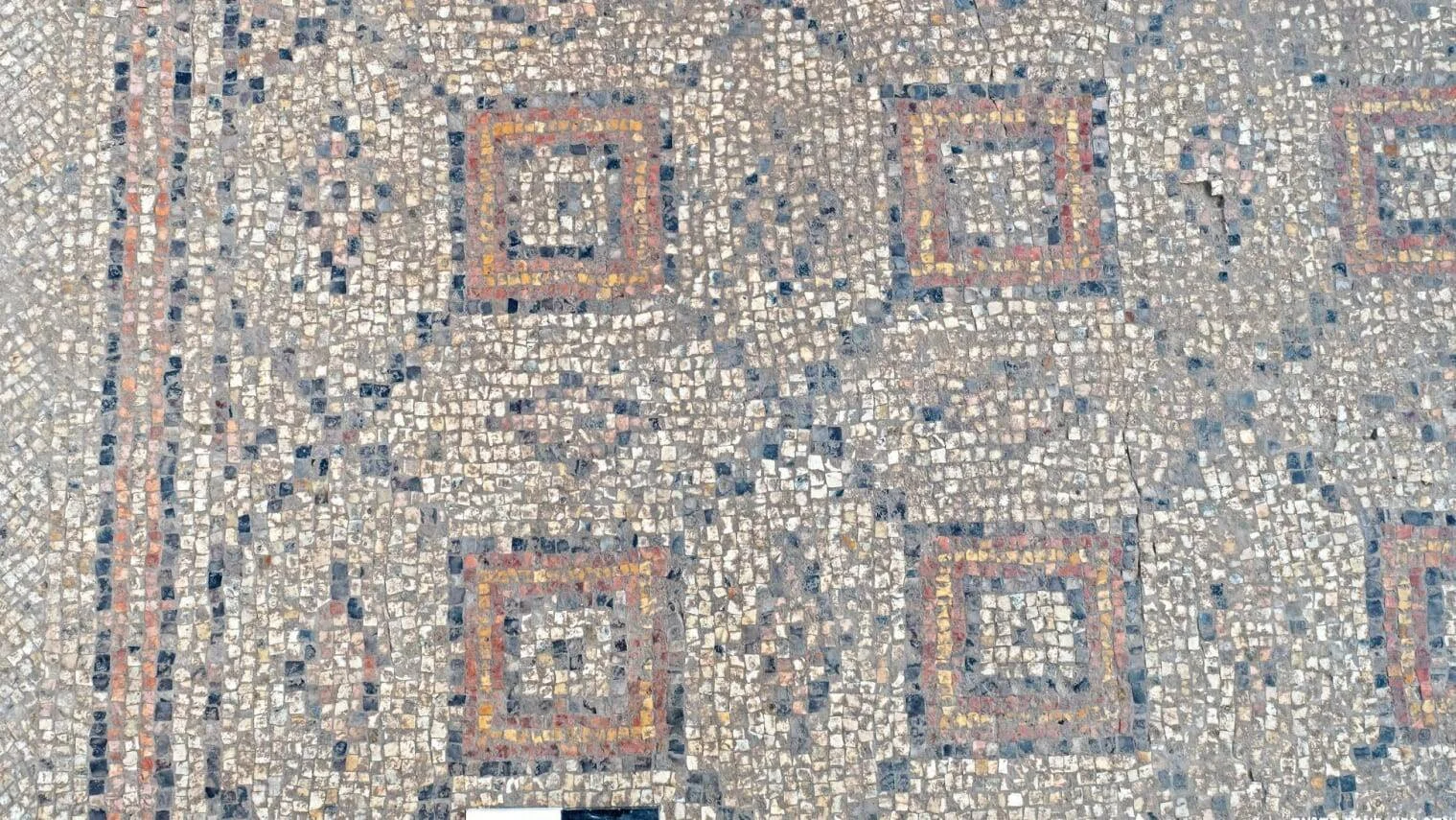 Suelo de mosaico antiguo compuesto por pequeñas teselas blancas, azules y rojas formando patrones geométricos cuadrados concéntricos.