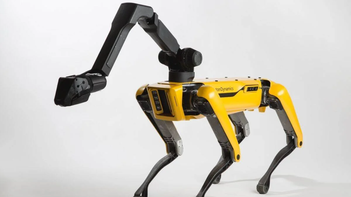 Robot cuadrúpedo amarillo y negro de Boston Dynamics con un brazo articulado montado en su lomo, sobre fondo blanco.
