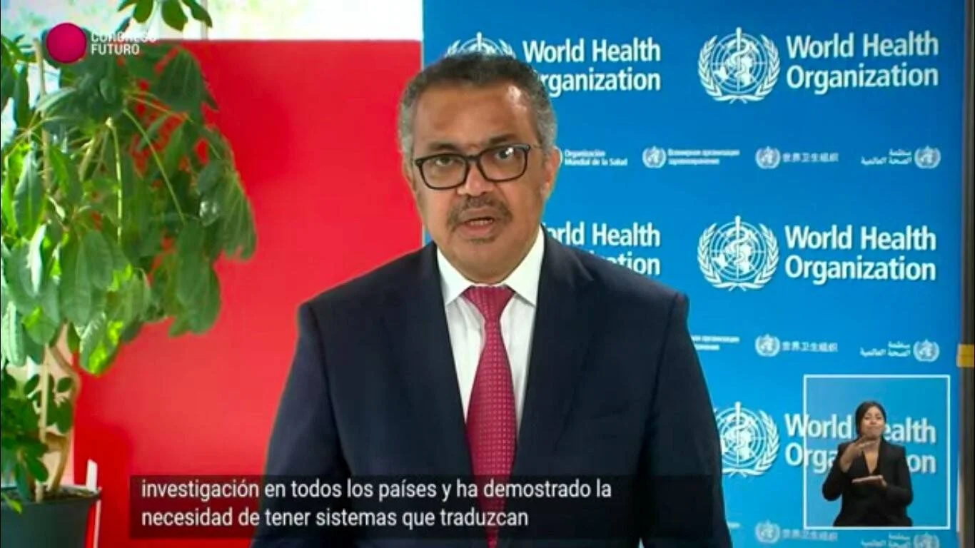 Hombre con traje y corbata roja habla frente a un panel de la Organización Mundial de la Salud durante una transmisión con subtítulos en español.