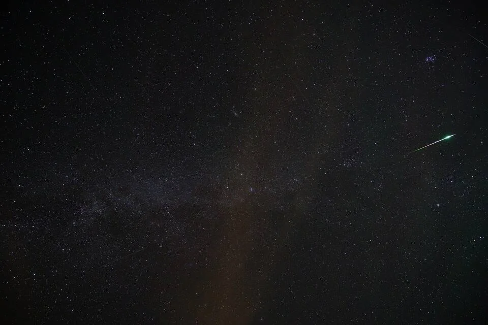 Un meteoro con estela verde atraviesa el cielo nocturno estrellado junto a la banda difusa de la Vía Láctea.