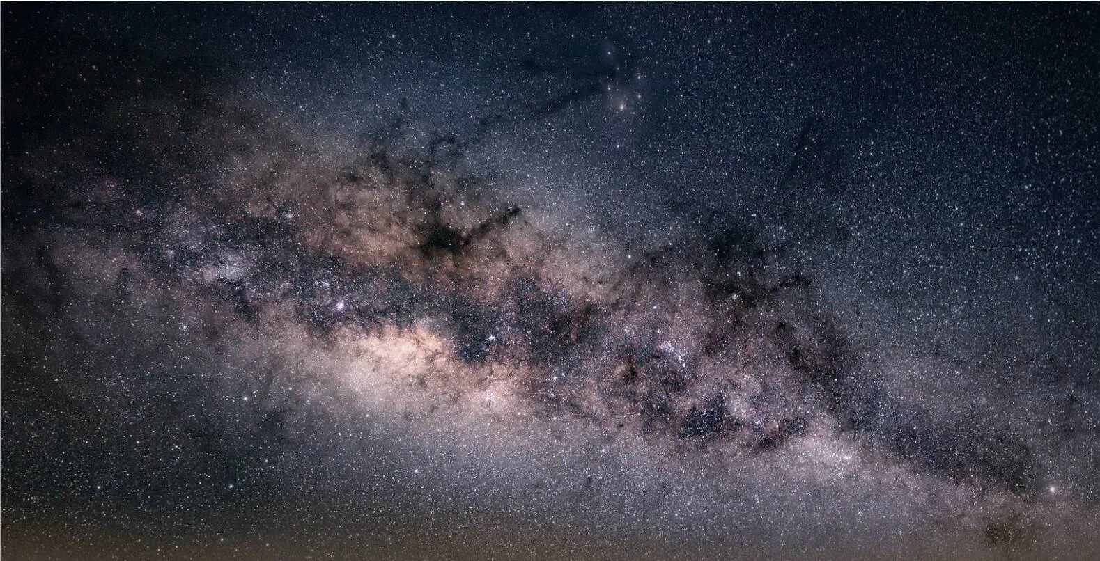 Panorámica del núcleo de la Vía Láctea con miles de estrellas, nubes de polvo cósmico y nebulosidades en tonos azules y dorados.