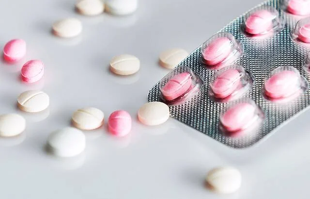 Blíster con comprimidos rosas y pastillas blancas dispersas sobre una superficie clara.