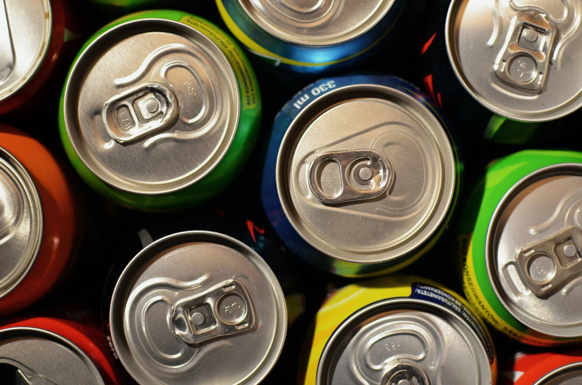 Vista cenital de múltiples latas de bebidas de aluminio de distintos colores con sus anillas de apertura visibles.