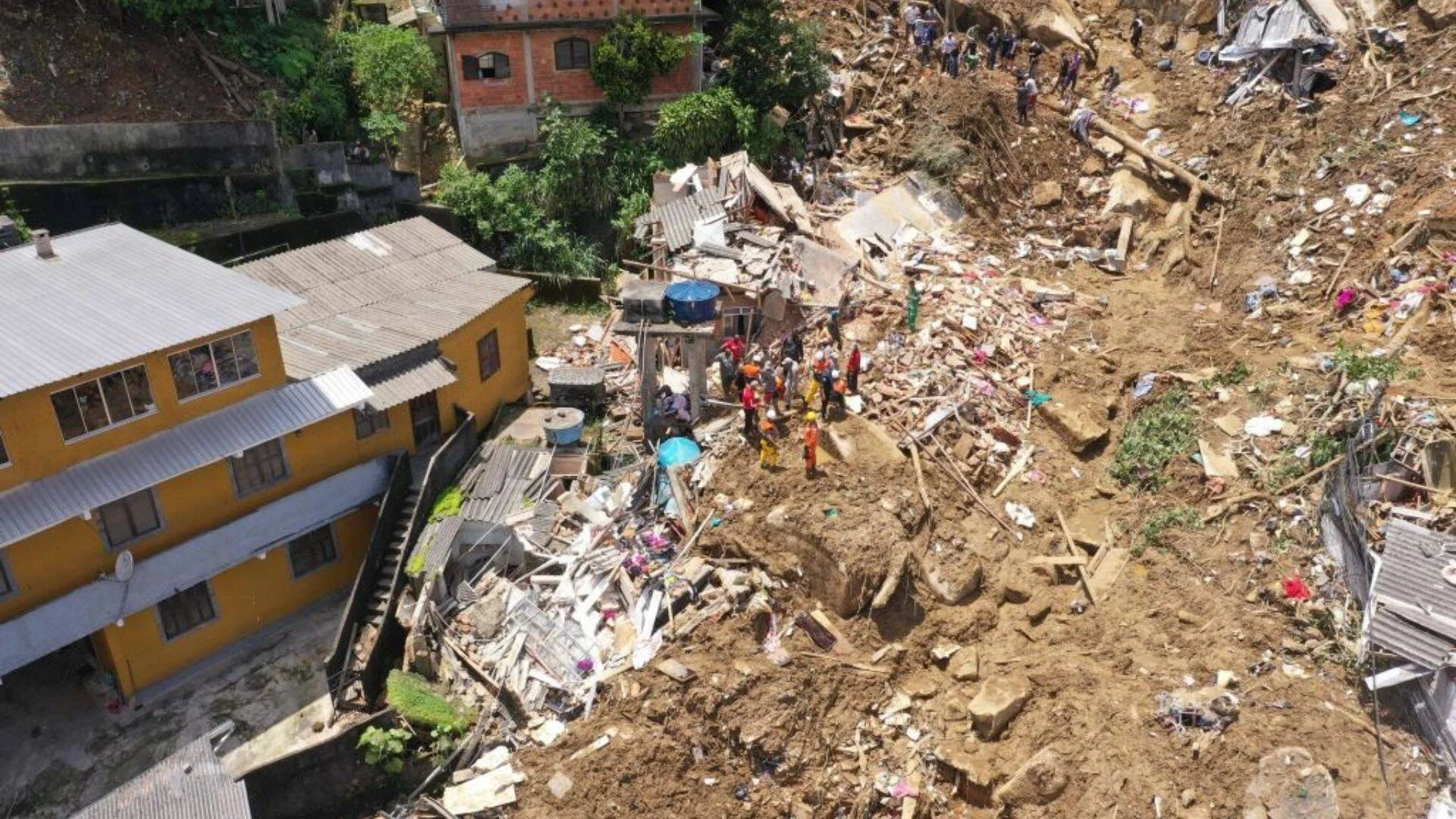 Vista aérea de un deslizamiento de tierra que destruyó varias casas; equipos de rescate trabajan entre los escombros y el barro.