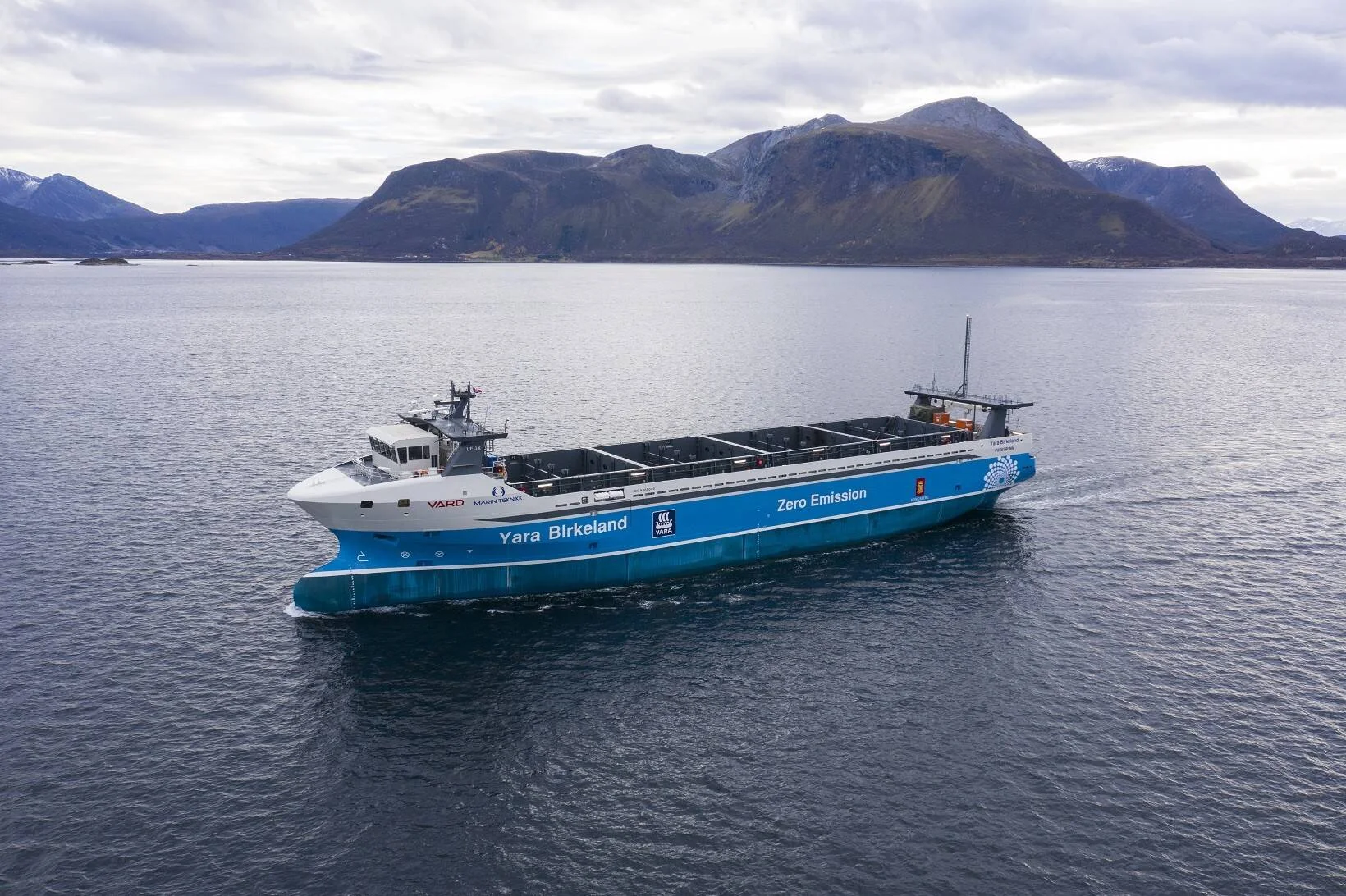 El barco de carga autónomo y eléctrico Yara Birkeland, con inscripción 'Zero Emission', navega por un fiordo noruego rodeado de montañas.