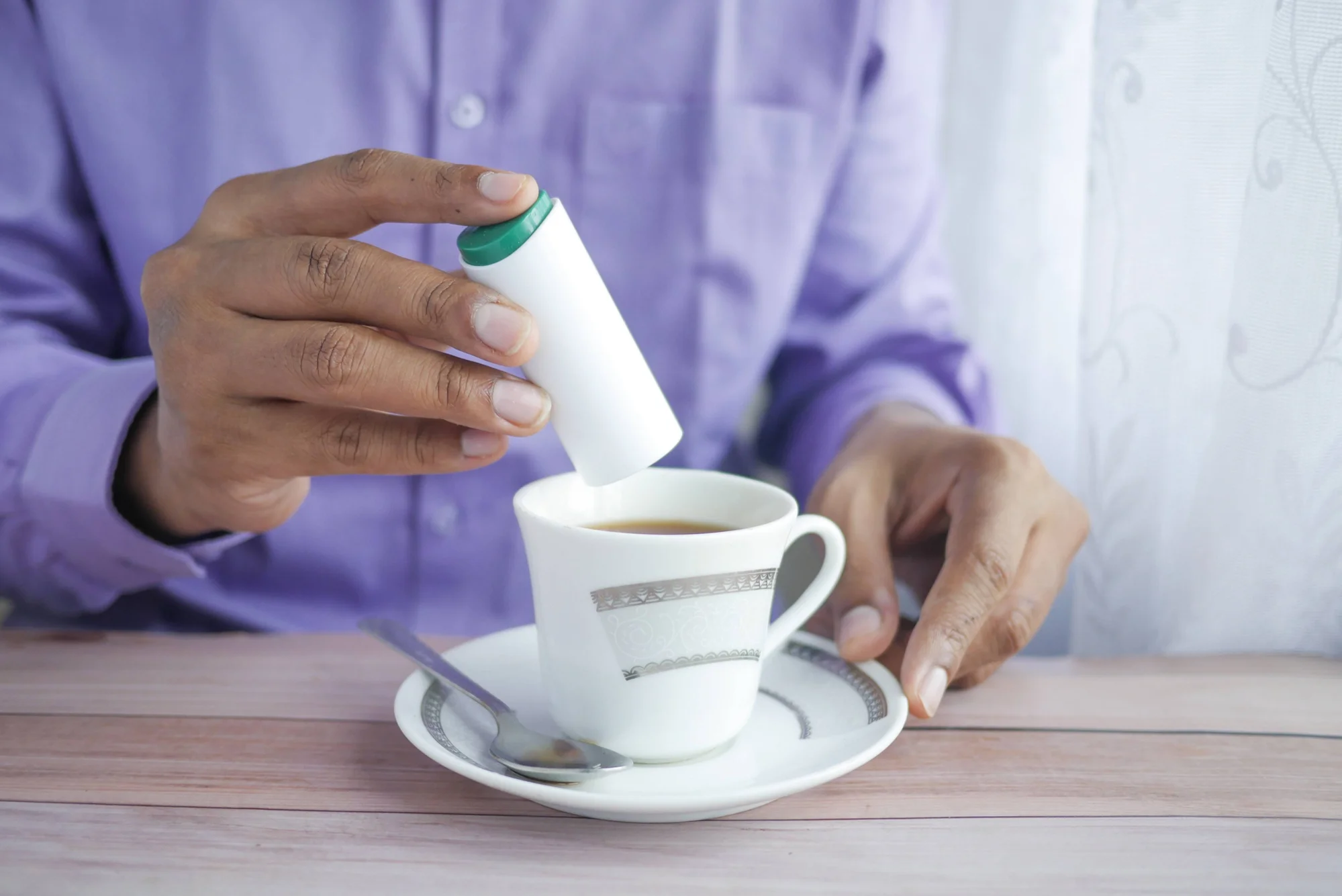 Una persona vierte edulcorante líquido desde un dispensador blanco con tapa verde en una taza de café.