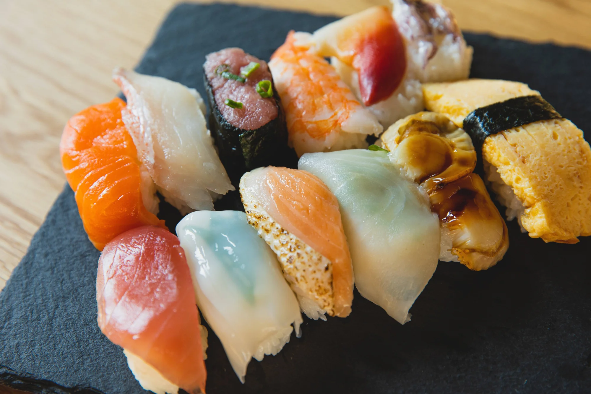 Selección de piezas de nigiri sushi con salmón, atún, gamba, erizo y tortilla japonesa sobre tabla de pizarra negra.