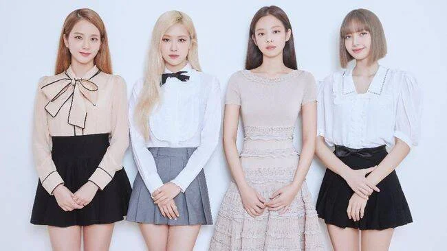 Cuatro jóvenes mujeres con outfits elegantes en blanco y negro posan juntas frente a fondo blanco.