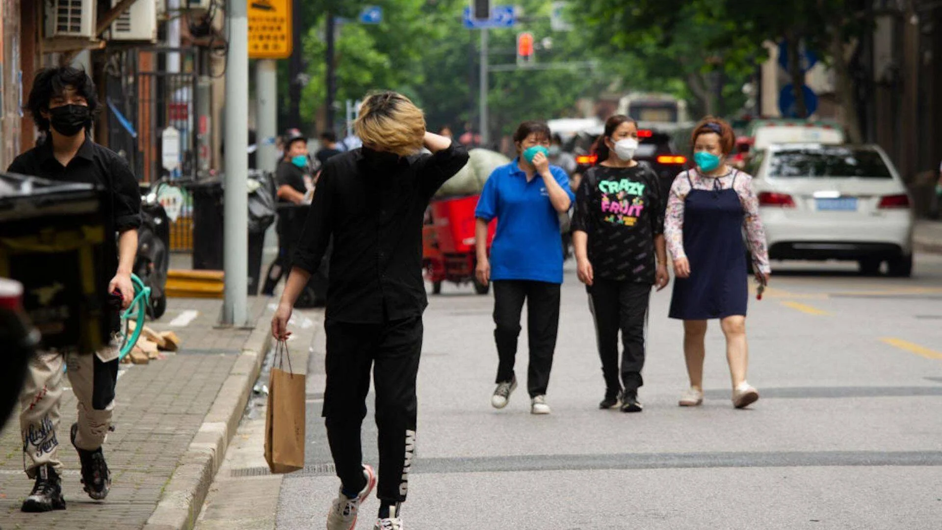 Varias personas con mascarillas sanitarias caminan por una calle urbana de una ciudad china.