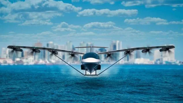 Vehículo aéreo eléctrico de despegue vertical rasando la superficie del mar frente a un horizonte urbano.