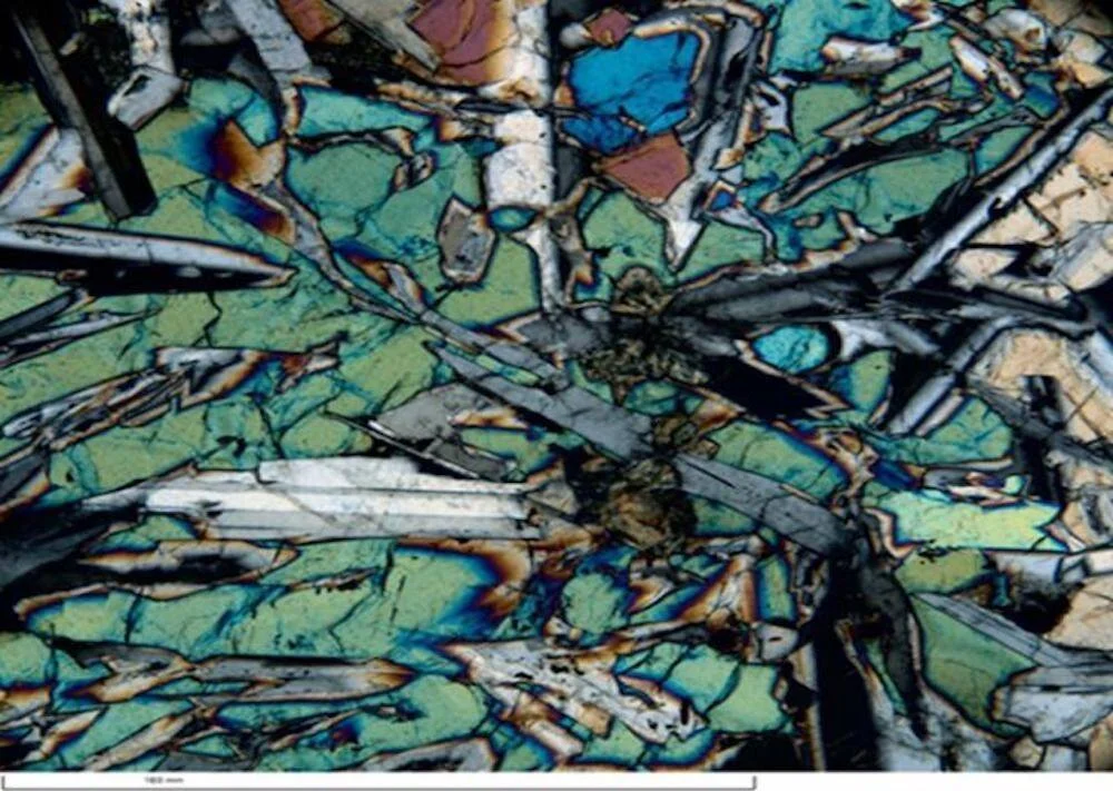 Cristales minerales con colores de interferencia azules, verdes y dorados observados en microscopio de luz polarizada.